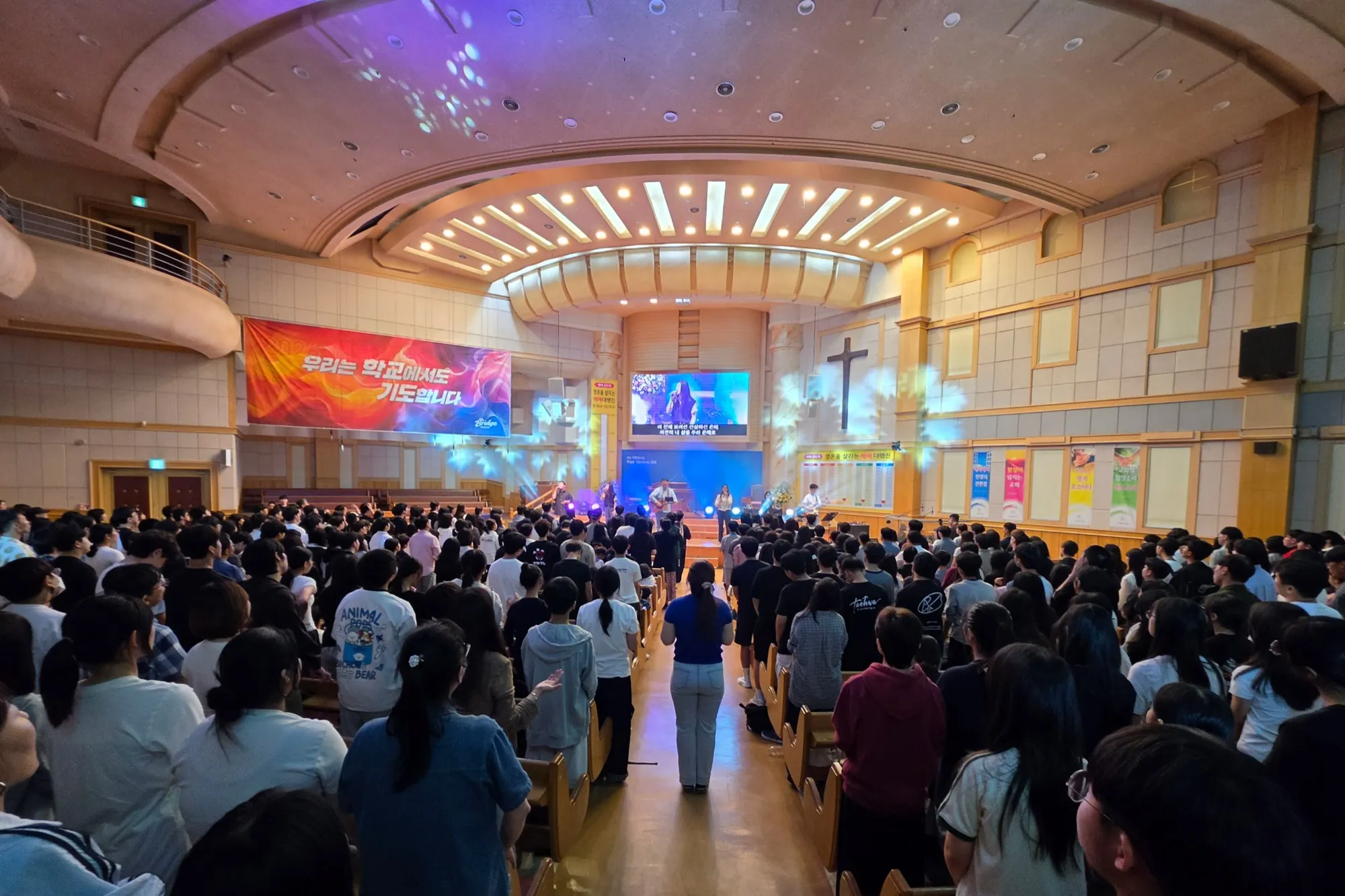 A sanctuary full of teenagers, seen from the back, with the stage and students singing